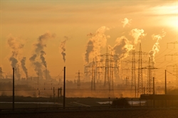 [ai] Industrial landscape at sunset with multiple smokestacks emitting steam and smoke, and high voltage power lines in the foreground. The sky is illuminated in warm orange tones.