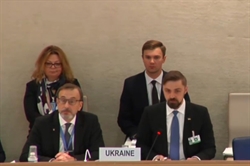 [ai] A group of officials from Ukraine seated at a conference table, with one man speaking into a microphone labeled 'Ukraine'. Other attendees are seated in the background, listening attentively.