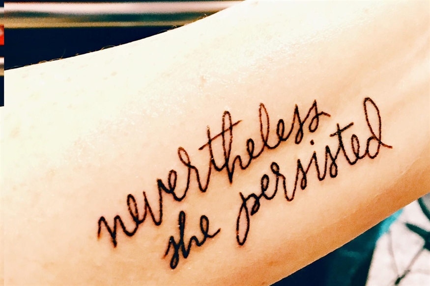 [ai] A tattoo on a person's forearm displaying the phrase 'nevertheless she persisted' in cursive font.