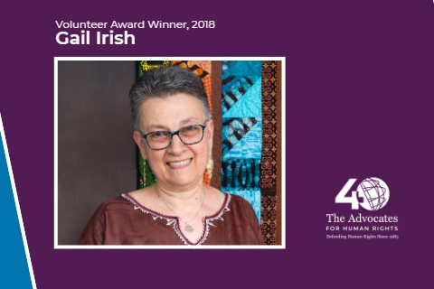 [ai] A portrait of Gail Irish, a woman with short gray hair wearing glasses and a brown blouse, smiling in front of a colorful patterned background. The image includes text indicating she is the Volunteer Award Winner for 2018.