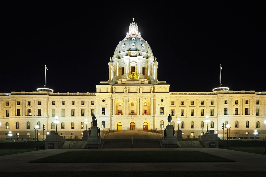[ai] The Minnesota State Capitol building illuminated at night, showcasing its ornate architecture. The central dome is prominently lit, while statues and lampposts are visible in the foreground.